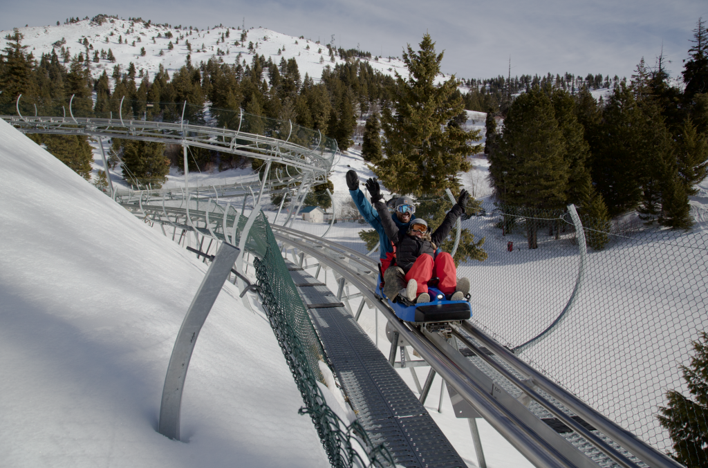 Two people riding the Glade Runner Mountain Coaster surrounded by snow-covered landscapes and a forest of trees at Bogus Basin Mountain Recreation Area.