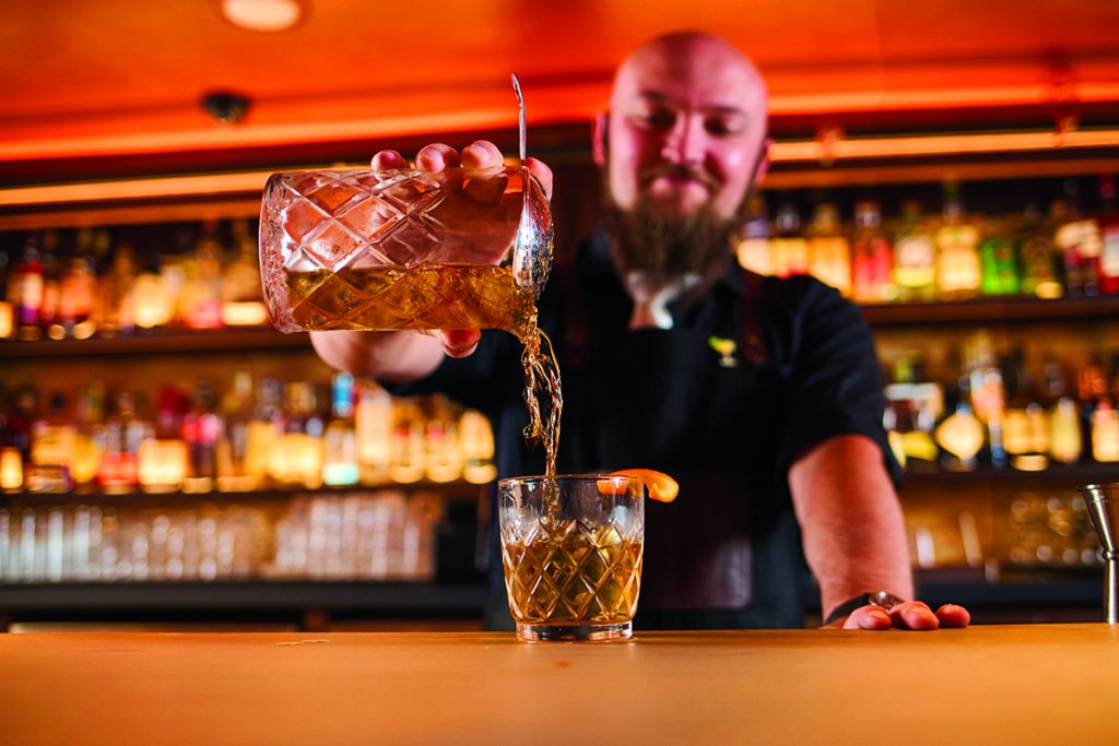 Bartender pouring a cocktail with an orange slice on the rim at Soiled Dove in Idaho Falls.