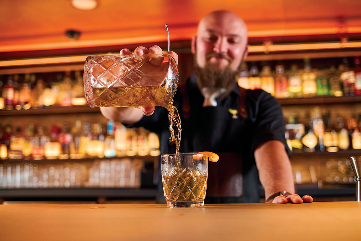 Bartender pouring a cocktail with an orange slice on the rim at Soiled Dove in Idaho Falls.