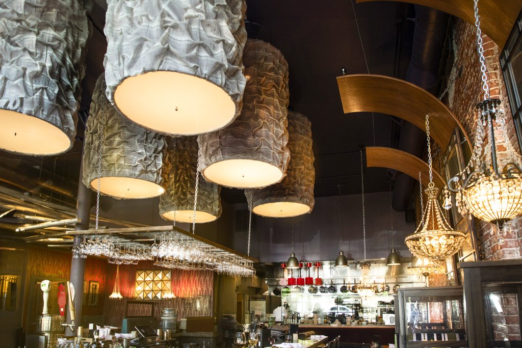 The interior of the ÁLAVITA restuarant, showing ornate ceiling fixtures hanging above the dining room, and in the background, an open kitchen.