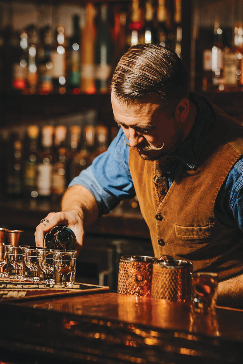 A bartender with a mustache and vest pours liquor into glasses at Press & Pony in Boise.