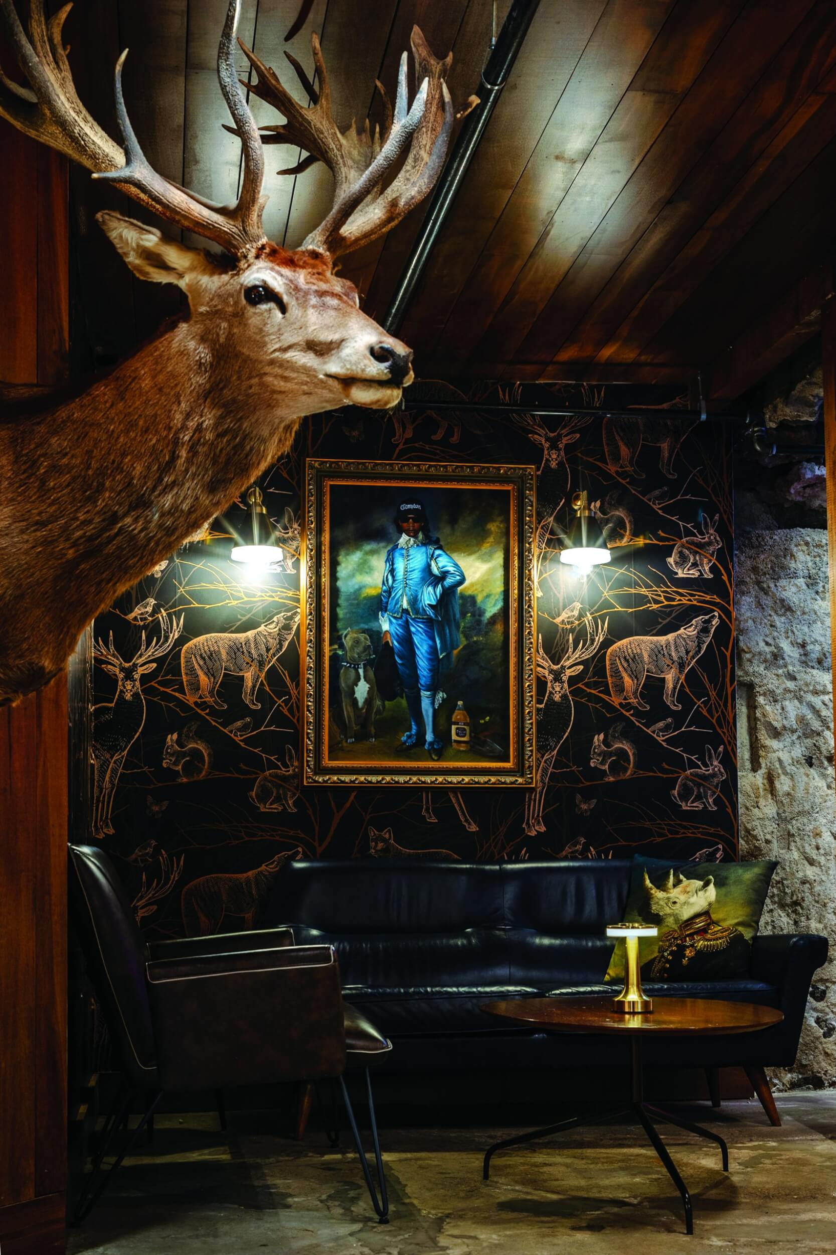 Interior of the eclectic Sick Stag in Nampa, featuring a taxidermy deer with antlers, animal wallpaper, a painting on the wall, and a hippo pillow on the couch.