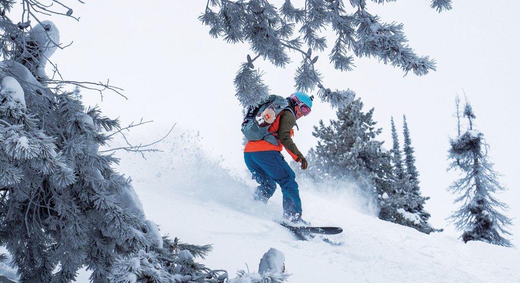 A snowboarder wearing a backpack sends snow flying as he moves between trees on Magic Mountain.