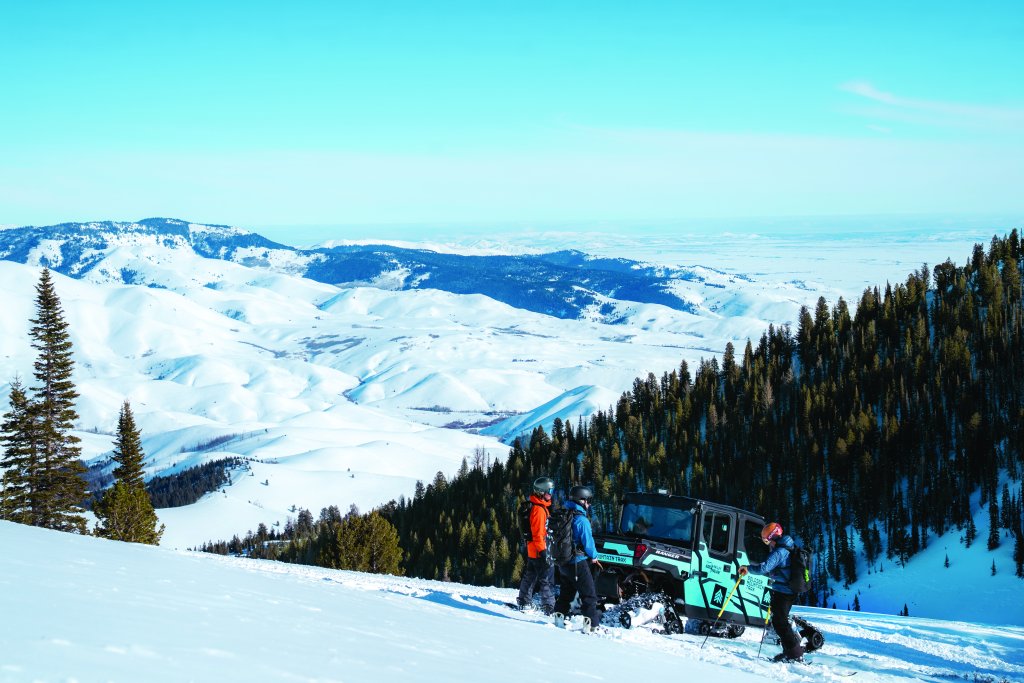 Snowboarders congregating around a TRAX skiing machine in the backcountry of Soldier Mountain.