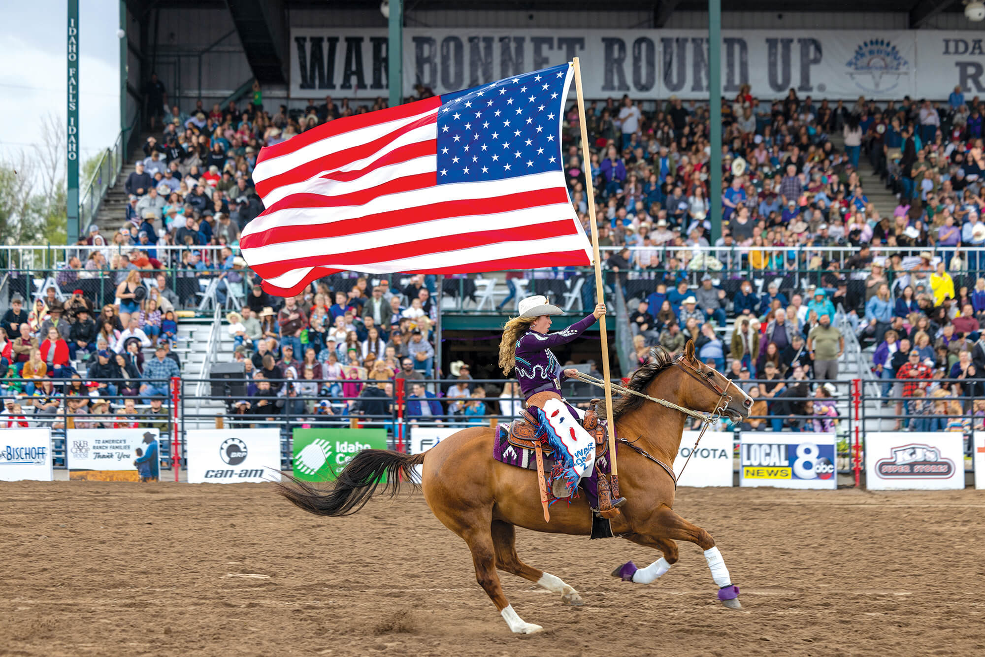 A cowgirl holds an American Flag as she rides a horse during the Grand Entry at the War Bonnet Round Up in Idaho Falls.