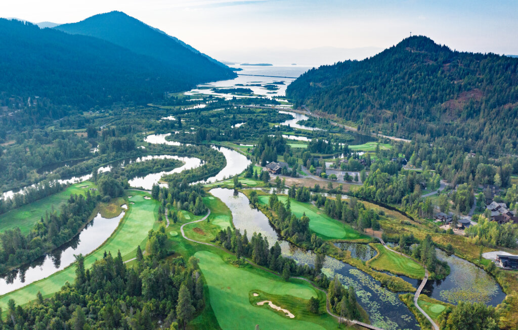 Aerial view of The Idaho Club golf course, with fairways and greens winding along the Clark Fork River delta and Lake Pend Oreille, framed by forested mountains.